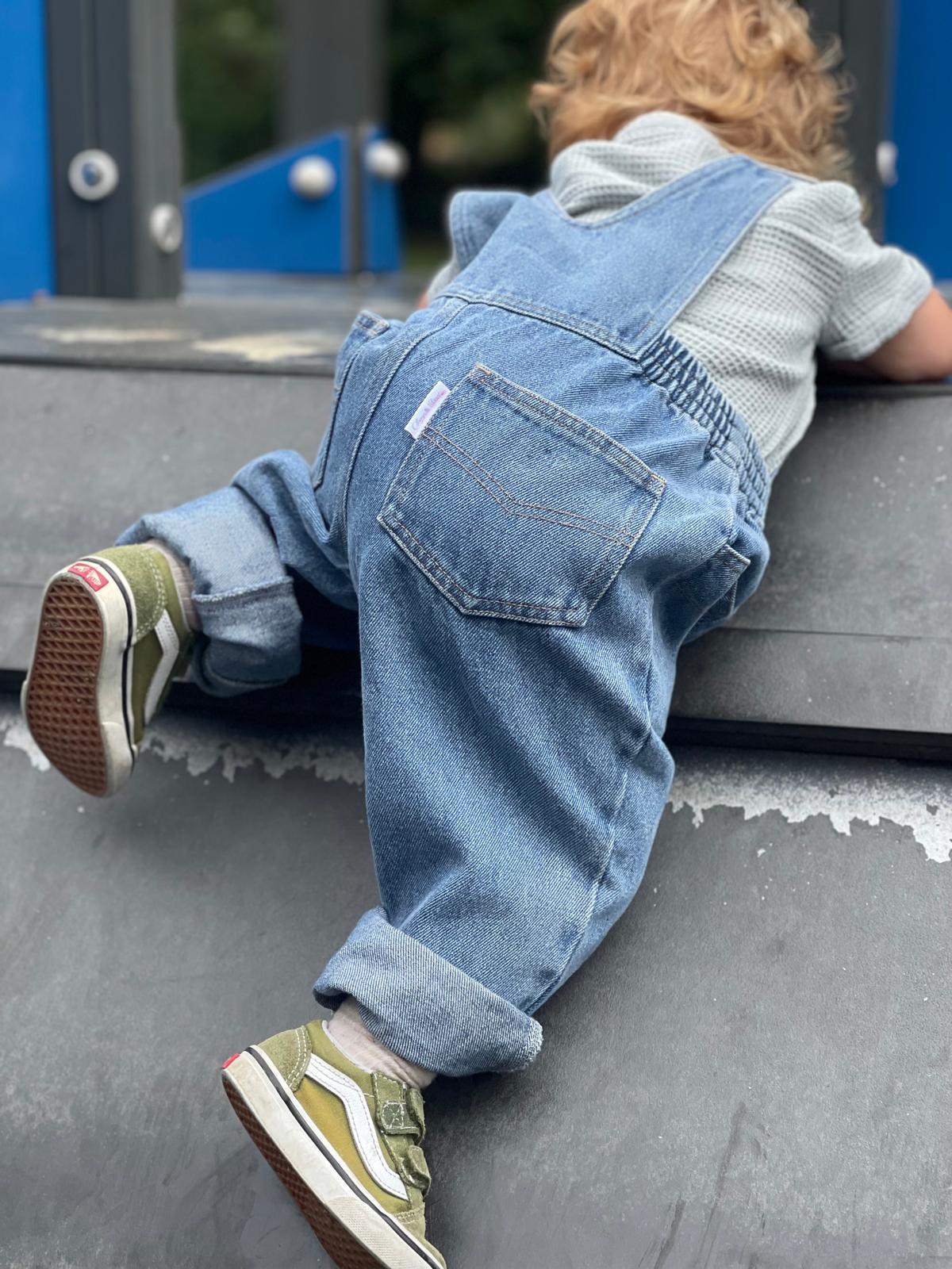 Enfant 2 ans en salopette bleu jean vintage de dos en train de grimper