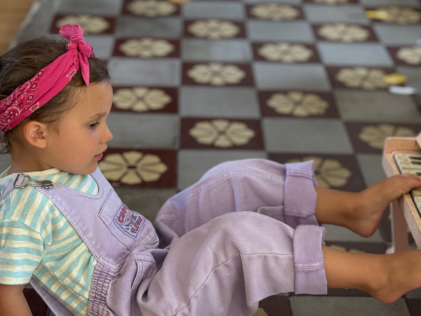 Enfant 3 ans en salopette mauve jouant du piano avec ses pieds