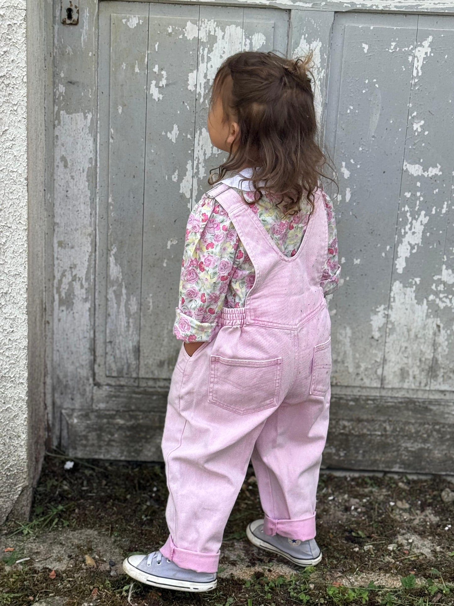 Enfant 3 ans en salopette rose trois quart dos.