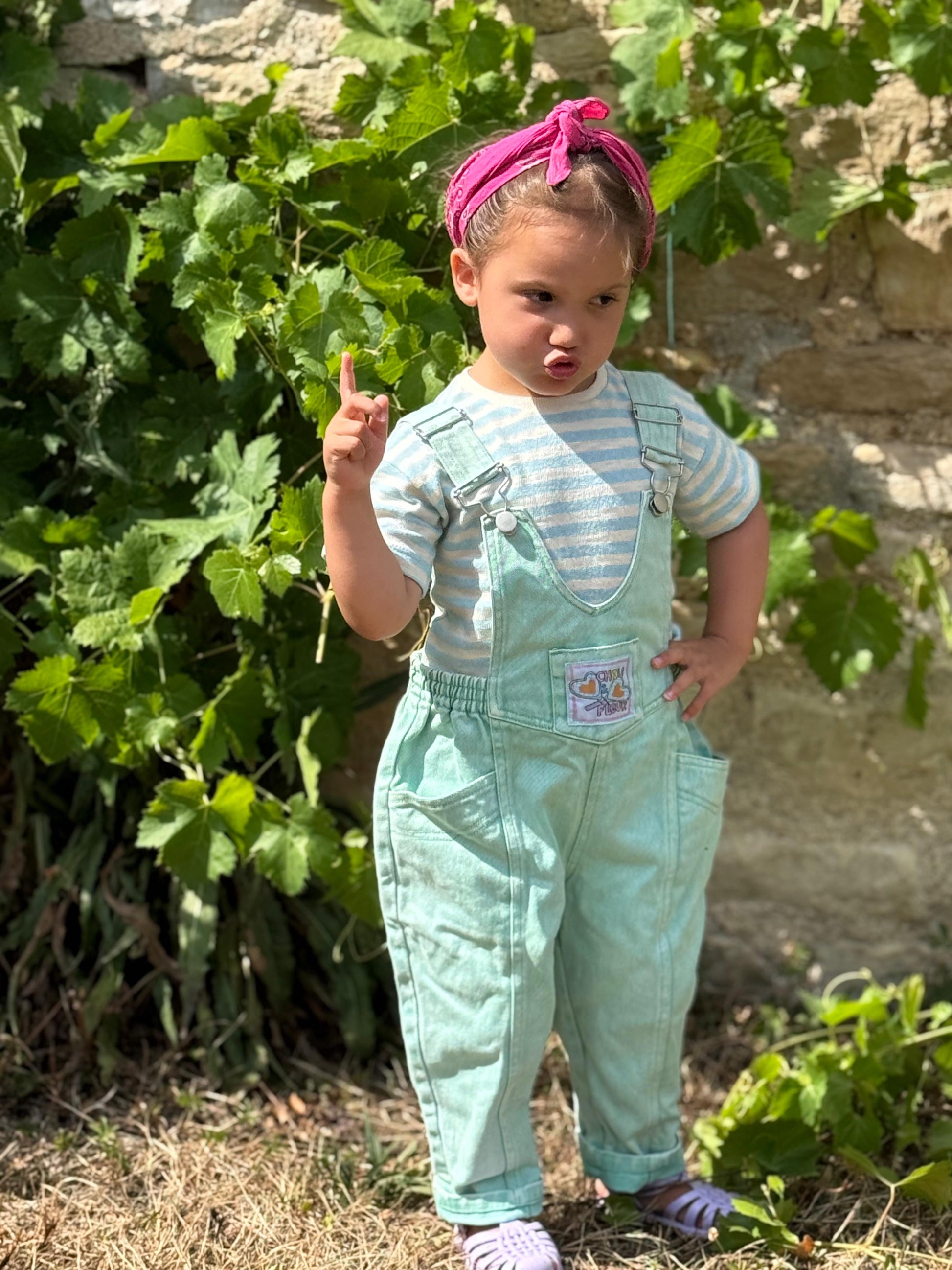 Enfant 3 ans en salopette verte le doigt levé, mains sur la hanche
