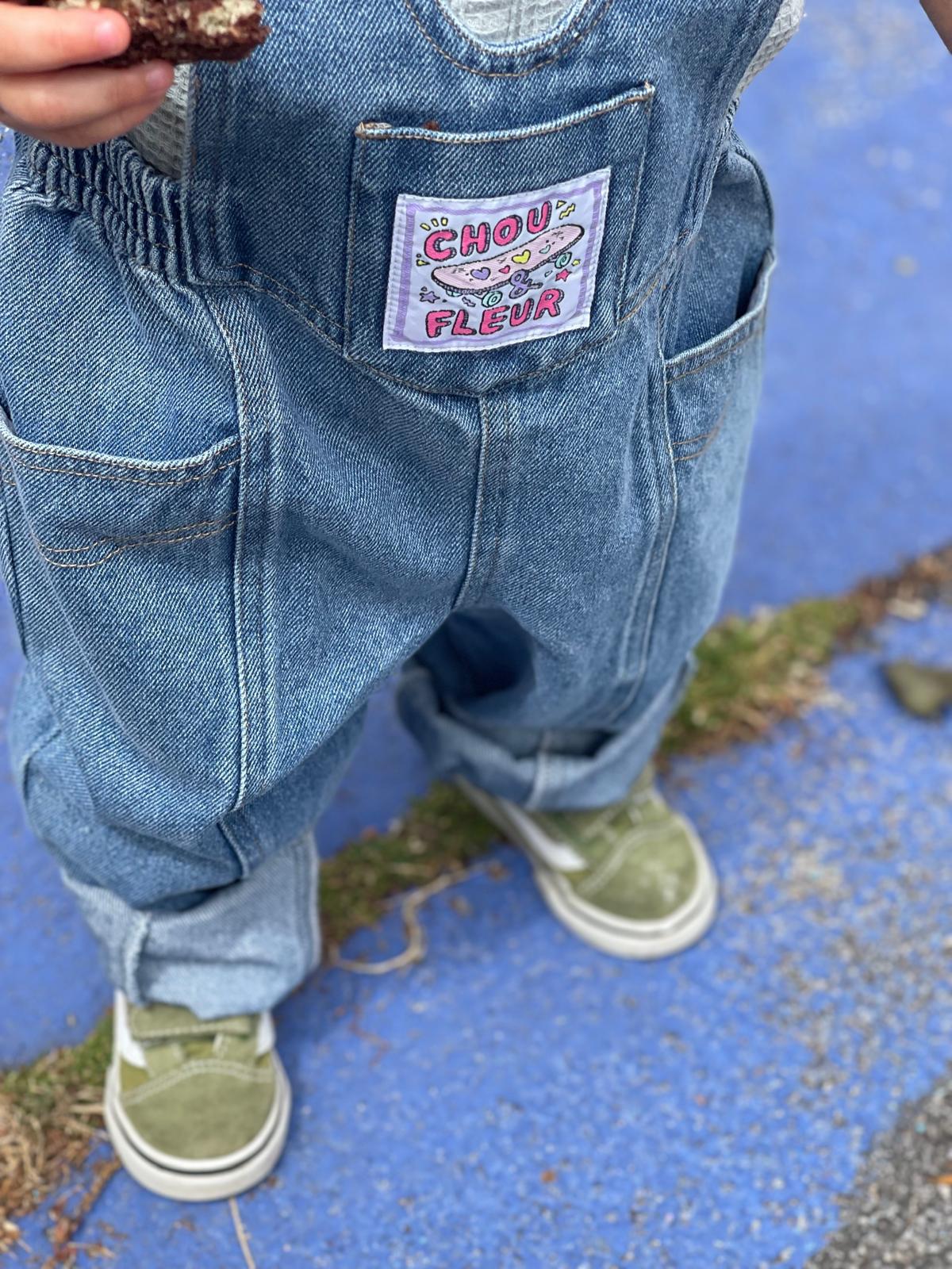 Zoom sur étiquette tissée de salopette en jean portée par enfant 2 ans