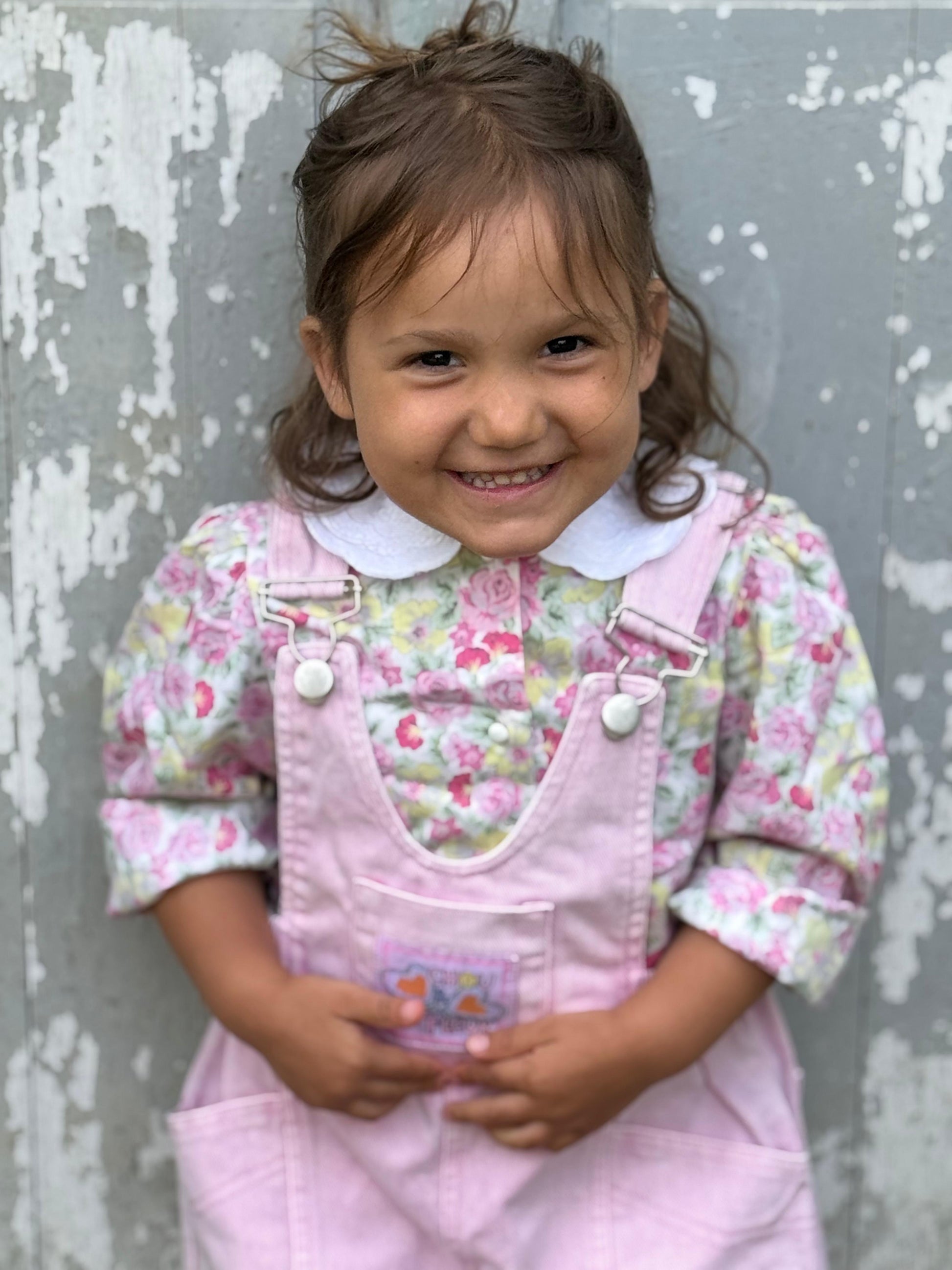 Enfant 3 ans assise et souriante en salopette rose vintage
