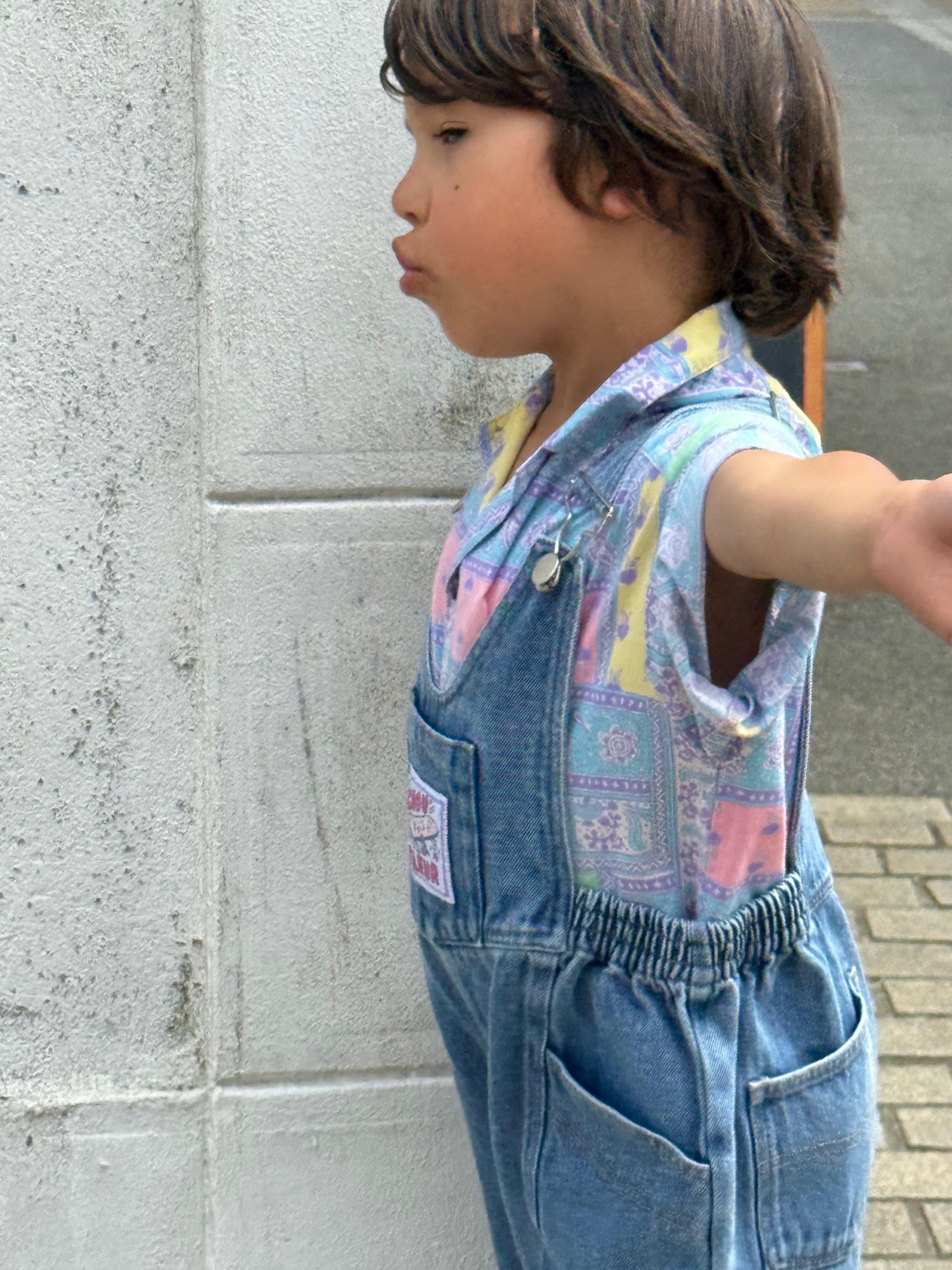 Garçon 5 ans bras ouverts de profil en salopette bleu jean vintage