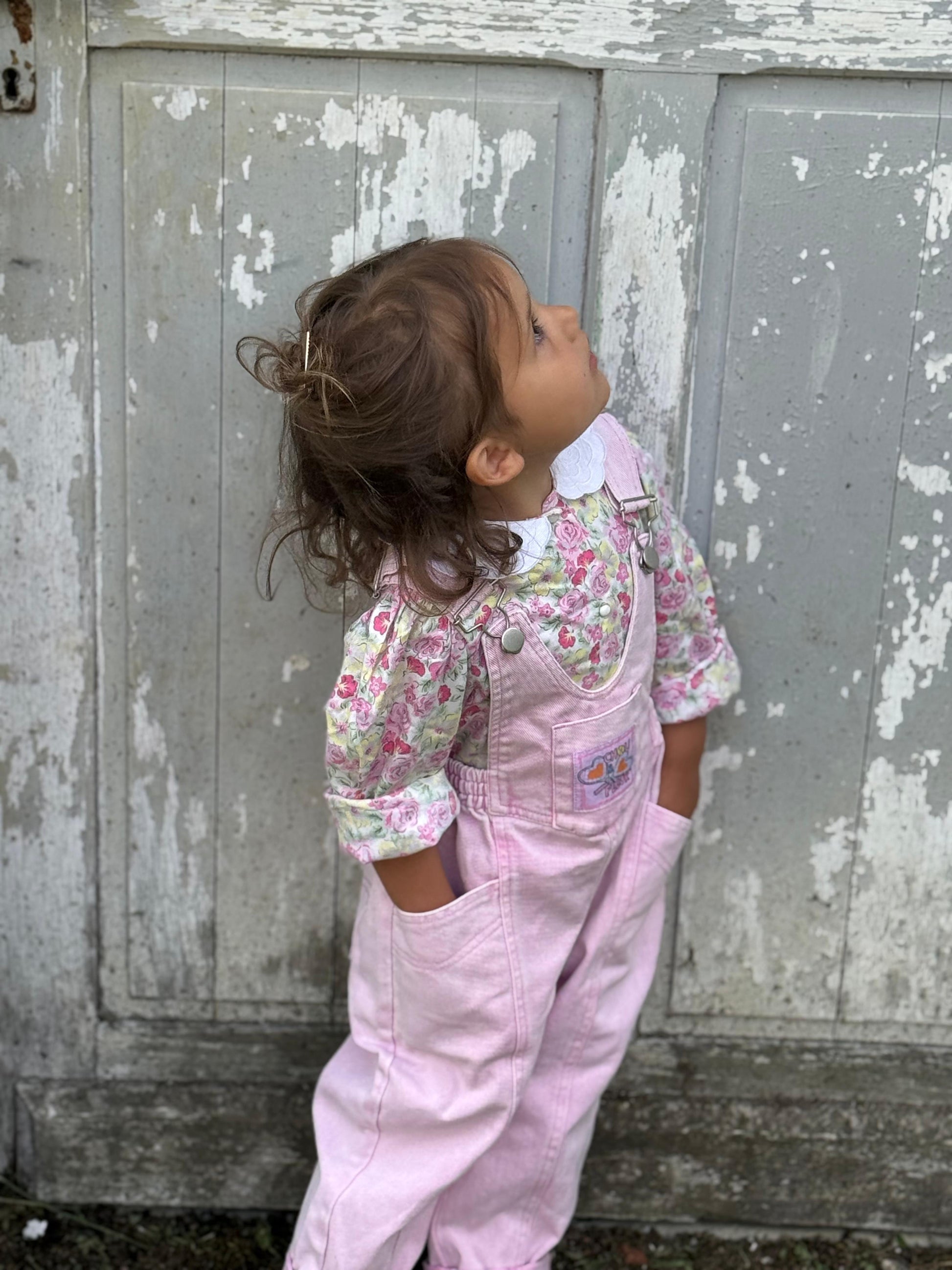 Enfant 3 ans en salopette rose vintage main dans les poches regardant en l'air de coté