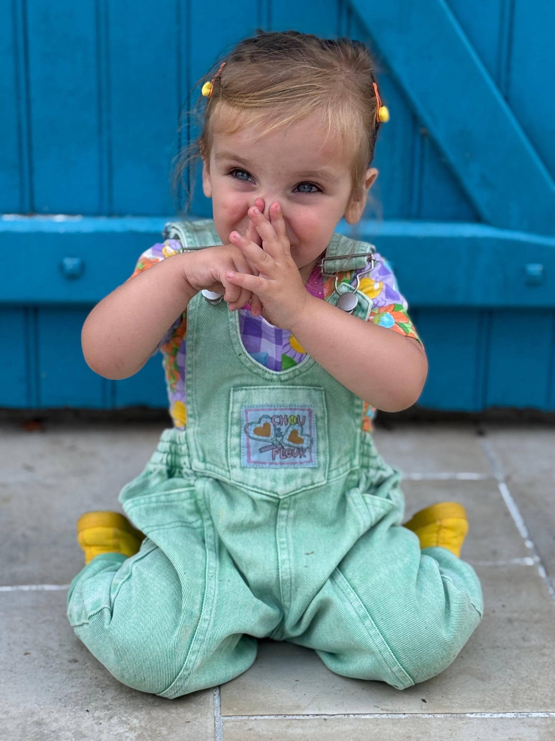 Fille 2 ans en salopette verte à genoux