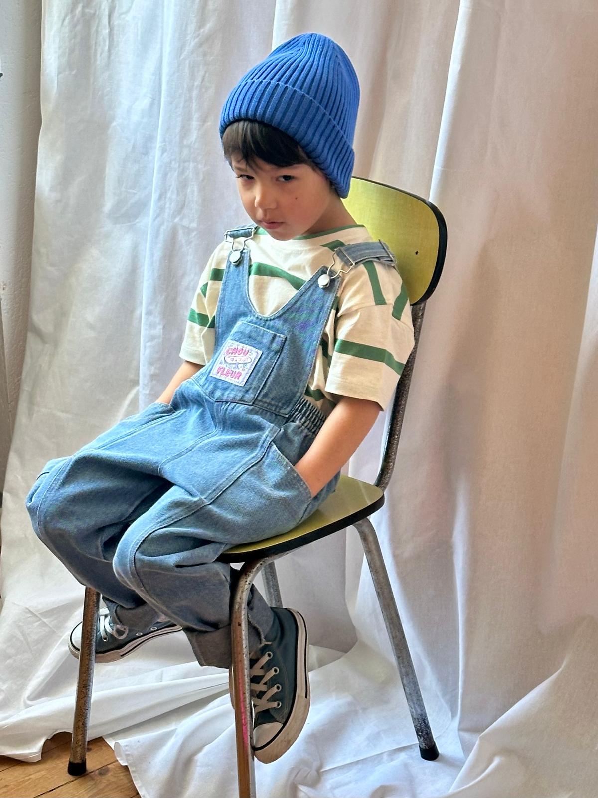 Look casual enfant : salopette en denim bleu et pull rayé vert, assis sur un banc — mode confortable et stylée