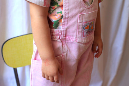 Zoom sur la salopette rose vintage pour enfant avec étiquette tissée 'Chou et Fleur' sur la poche avant